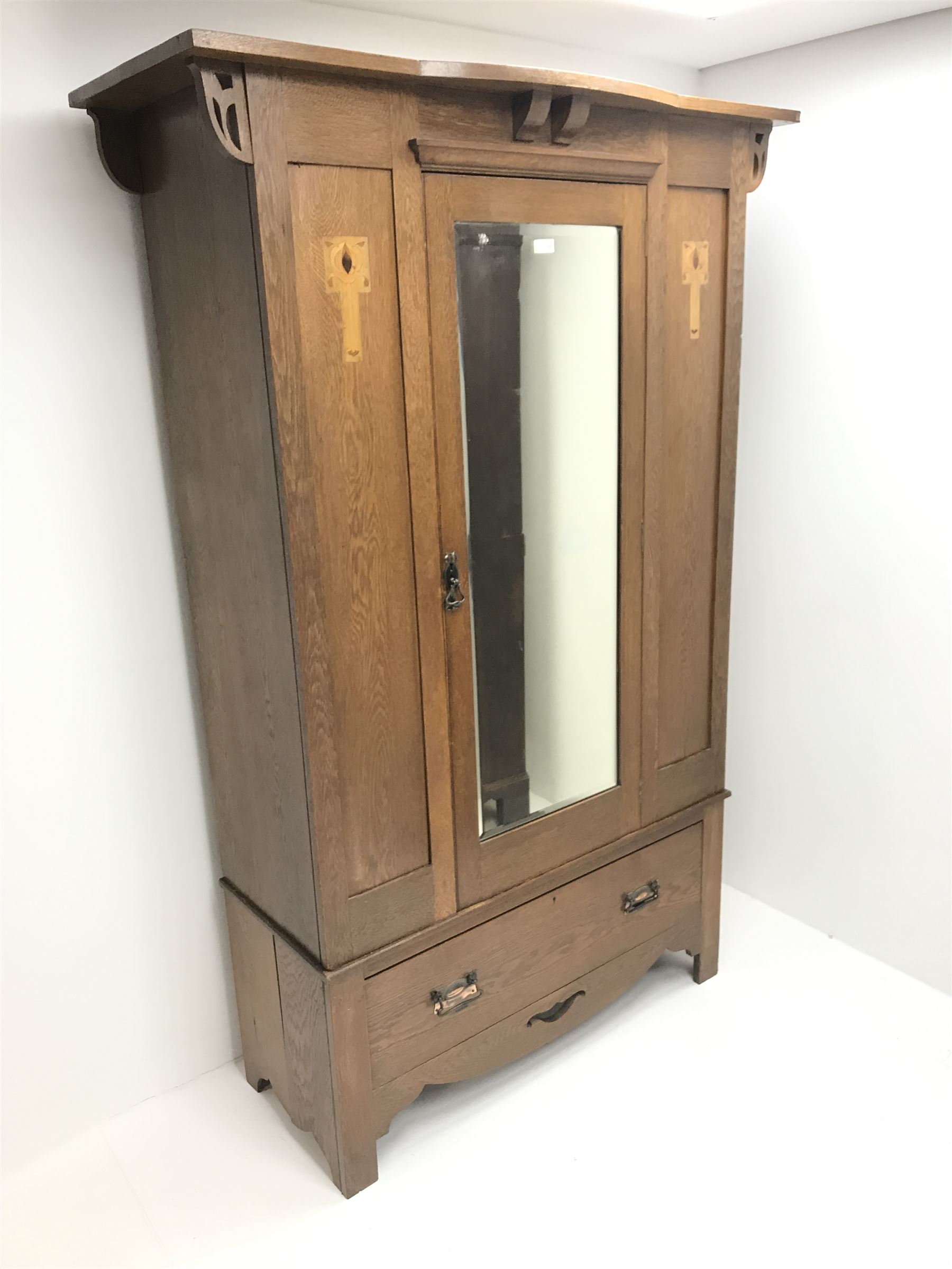 Arts and Crafts period oak wardrobe, projecting shaped cornice, single bevel edged mirrored door above drawer