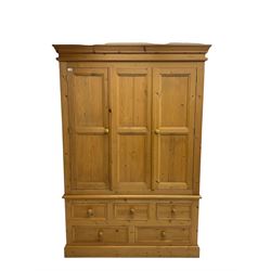 Pine triple wardrobe, enclosed by three panelled doors, fitted with five drawers, on skirted base