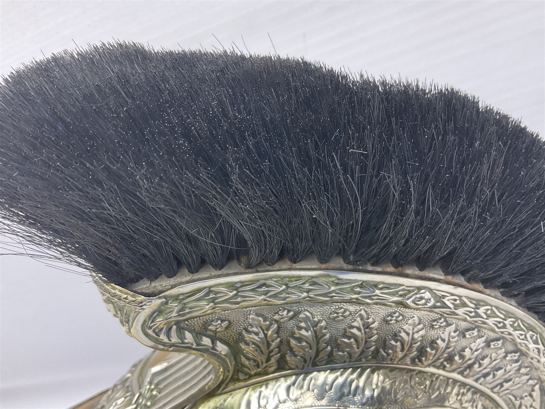 Early 20th century French mounted gendarme's helmet, brass with nickel-silver mountings, broad band embossed with fused grenade, high comb with the face of the gorgon Medusa at the peak and with a black horse hair crest, plume socket at the left, leather-backed nickel-silver chin scales with lion mask mounts.