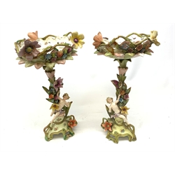 A pair of Continental porcelain centre pieces, the footed bases leading to a stems modelled with flowers, vines and putti, supporting baskets with conforming decoration, (one a/f), approx H40.