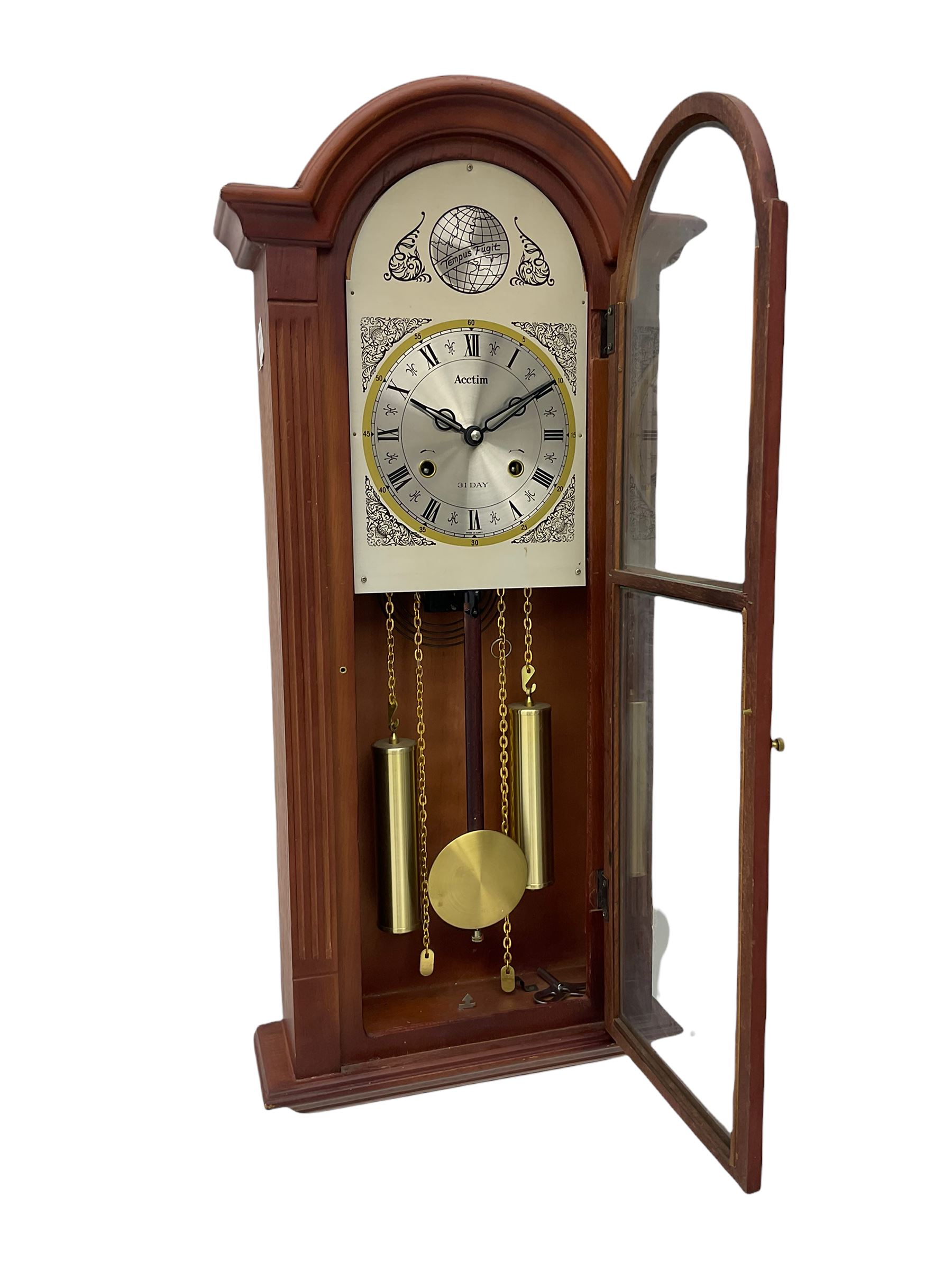 A contemporary Acctim (Anglo continental clock company) thirty-one day striking wall clock in a mahogany effect case with a fully glazed door displaying the pendulum and two dummy wights with chains, with a polished brass dial, Roman numerals, minute track and pierced steel hands, dial plate decorated with spandrels and Tempus Fugit inscribed on the dial brake-arch.
With key and pendulum.

