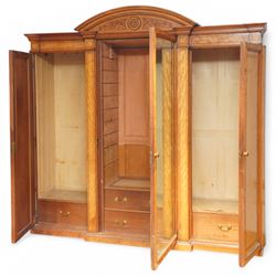 Victorian neoclassical style satinwood triple-section wardrobe, the central mirror section and arched pediment with carved monogram flanked by two panelled crossbanded doors, revealing two drawers and grooves for shelves, the hanging cupboards each with a single drawer, the whole supported on a plinth base