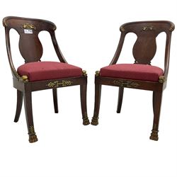 Pair of French Empire mahogany spoon0back side chairs, reeded cresting rail with scrolled ends over a shaped and pierced back splat, decorated with gilt metal mount in the form of winged classical maidens playing panpipes, drop-in seat upholstered in crimson lozenge patterned fabric flanked by gilt stylised scaled fish mounts, the apron with neoclassical gilt metal mounts, raised on sabre supports with paw feet