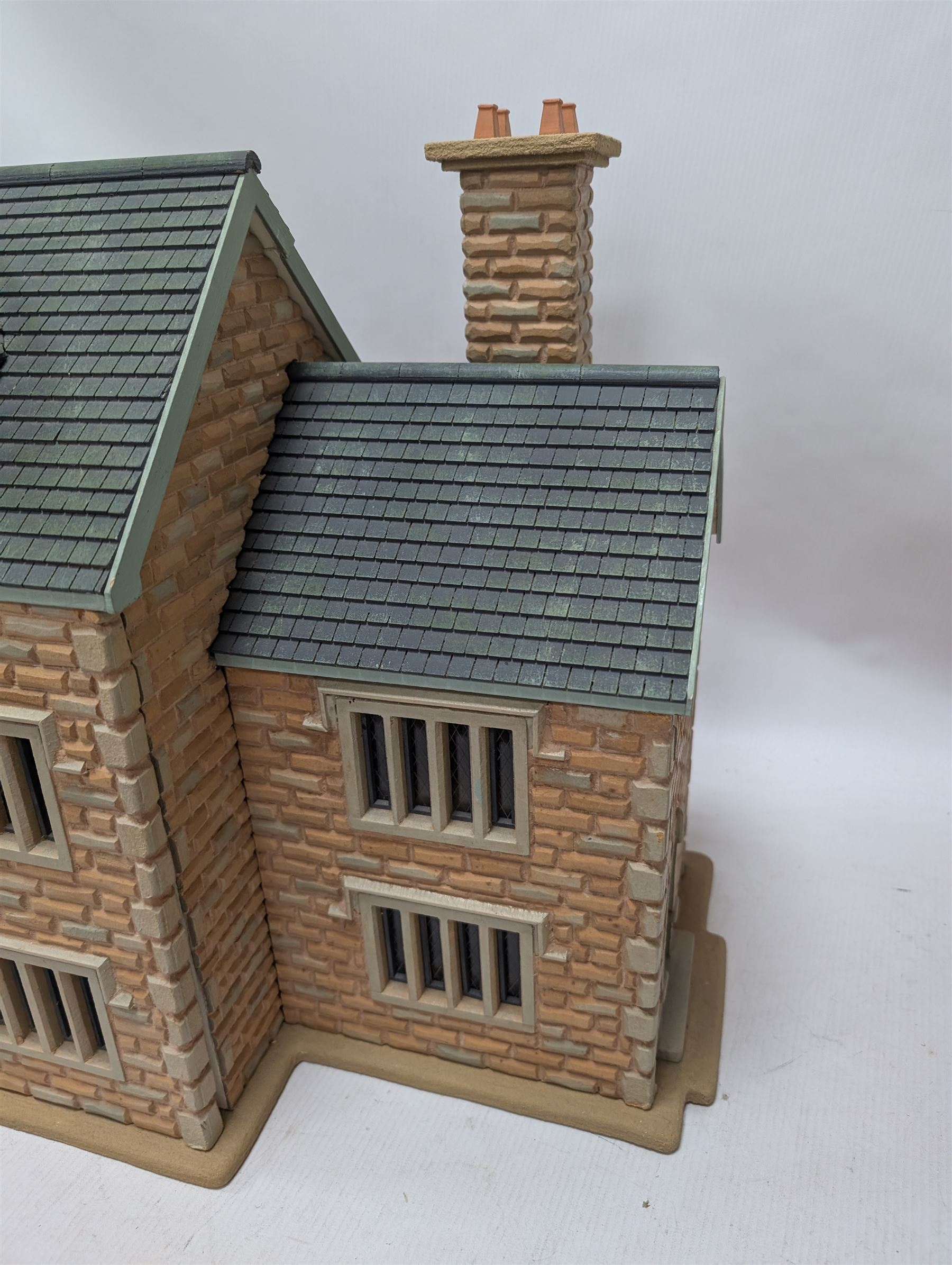 1:24 scale stone effect three-storey cottage dolls house, with green arched door and lattice effect windows, decorated to the interior with wooden floors, wired lighting and fire places, H45cm, W57cm, D26cm