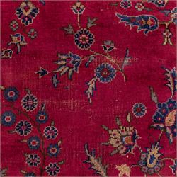 Large Persian-style mahal-type hand-knotted carpet, of rectangular form with a deep crimson field decorated with an all-over arrangement of stylized floral sprays and palmettes, with a central subtle medallion composition enclosed by a dark navy main border of scrolling floral motifs between narrow guard stripes with fringe ends 