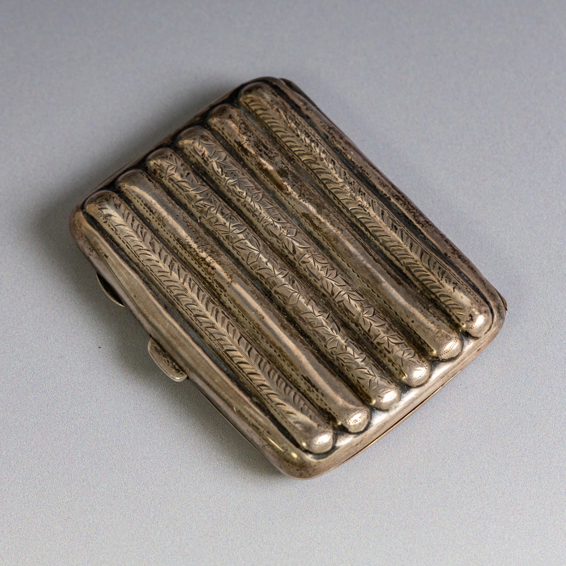 Two early 20th century silver cigarette cases, comprising a rectangular example with foliate decoration and vacant shield cartouche and a 1920s example with engine turned decoration and engraved initials, both hallmarked