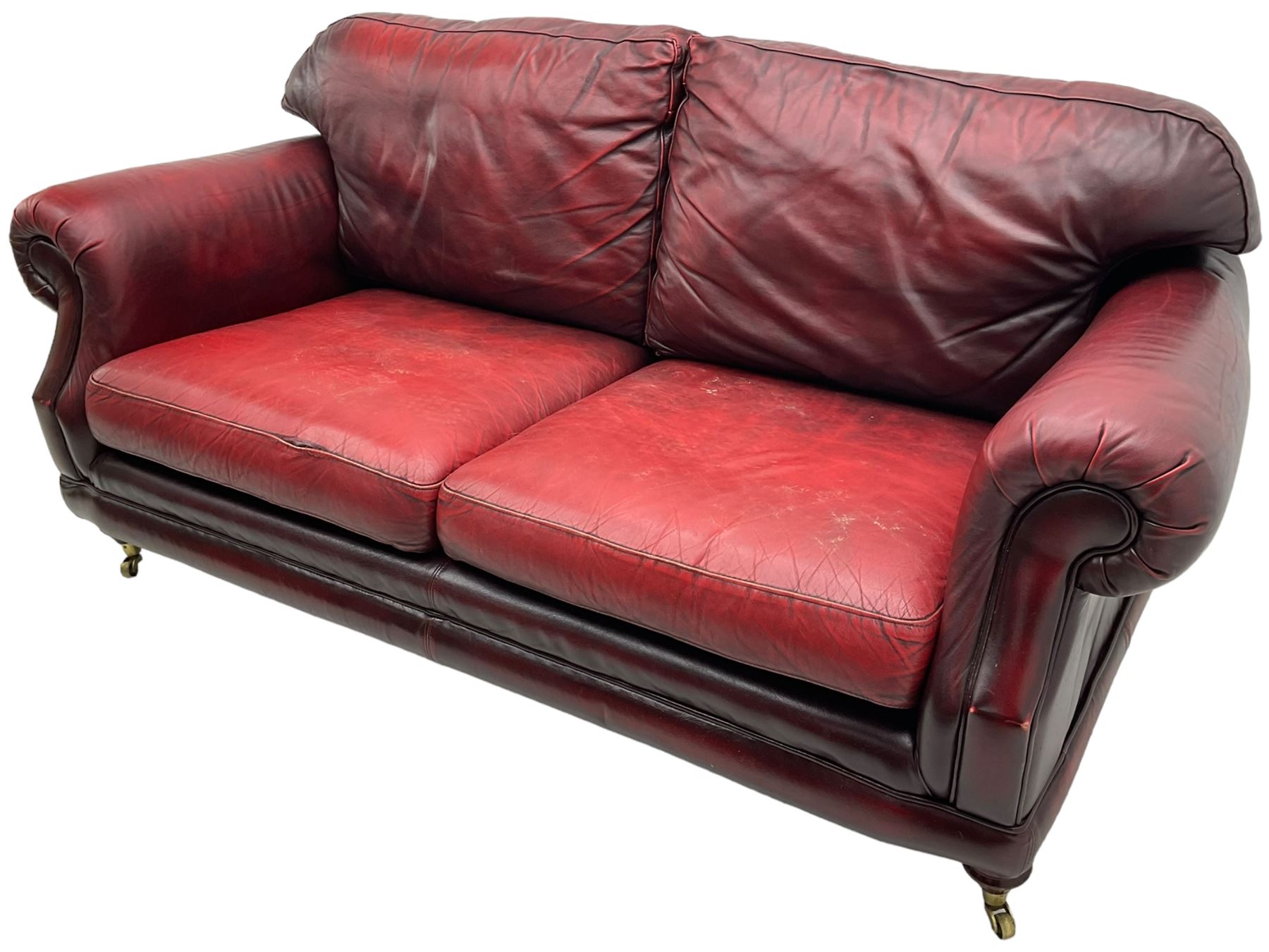 Thomas Lloyd - three-piece lounge suite, comprising of traditional shape two seat sofa (W190cm H80cm) and a pair of wingback armchairs (W100cm H91cm), each with rolled arms over turned supports with brass castors, upholstered in oxblood red leather