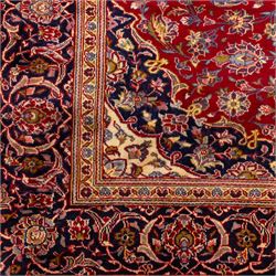 Central Persian Kashan hand-knotted rug, crimson red field with central ivory and indigo floral medallion surrounded by an all-over arrangement of finely drawn palmettes, flowering vines, and rosettes, with corresponding navy blue spandrels enclosed by a floral main border with multiple guard stripes, with cotton fringe ends    
