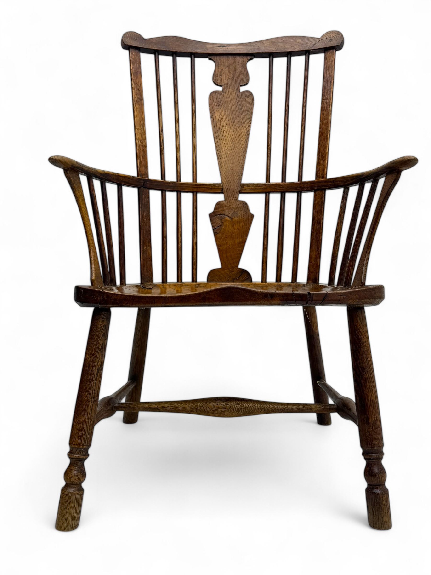 Early-to-mid 19th century elm and ash high-back Windsor armchair, central vase-shaped splat flanked by slender vertical spindles, outward-curving arms, shaped and dished saddle seat, raised on turned and splayed supports united by H-stretcher