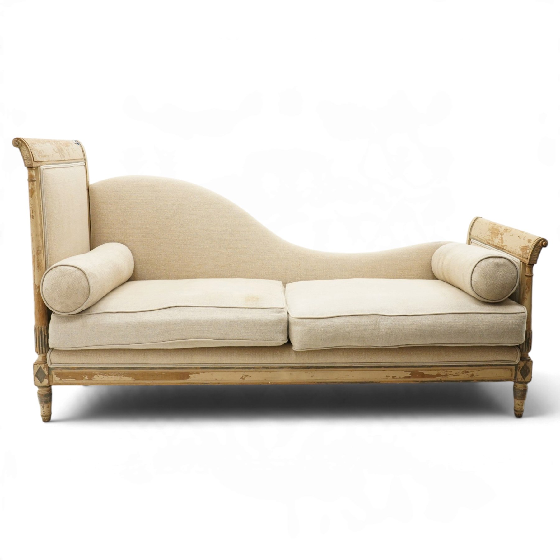 19th century French painted day bed, asymmetrical scrolled ends flanking a serpentine upholstered back, with upholstered end panels, loose seat cushions and cylindrical bolsters upholstered in beige fabric, with turned uprights with fluted detailing, moulded seat rail and lozenge-moulded corner blocks, raised on turned tapering supports