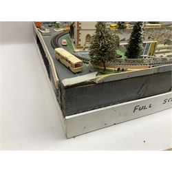 Table top 'N' gauge continental scenic layout as a split level town with various loops of track, station with numerous platforms, engine shed, assorted buildings, roads with motor vehicles and figures, tunnels, trees, river with bridge, tram depot etc 122 x 52cm