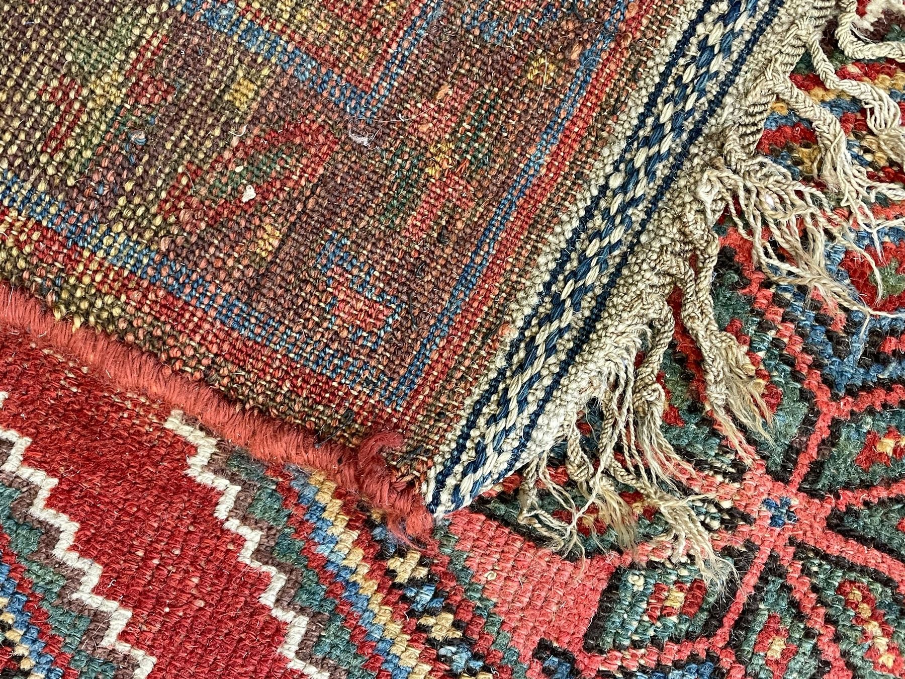Kurdish crimson ground rug, the field decorated with four lozenge medallions, triple band border decorated with stylised flower heads