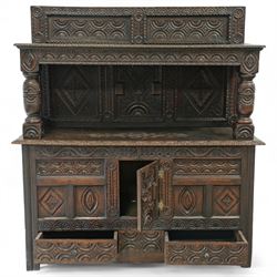 An early 20th-century Jacobean revival style carved oak Court Cupboard, tier-form of 17th-century design, rectangular form with carved back with geometric motifs and arches, projecting top section over twin baluster columns connecting the lower tier above a carved panelled front and panelled cupboard door with profusely carved lozenges and lunettes, above two base drawers, raised on block feet 