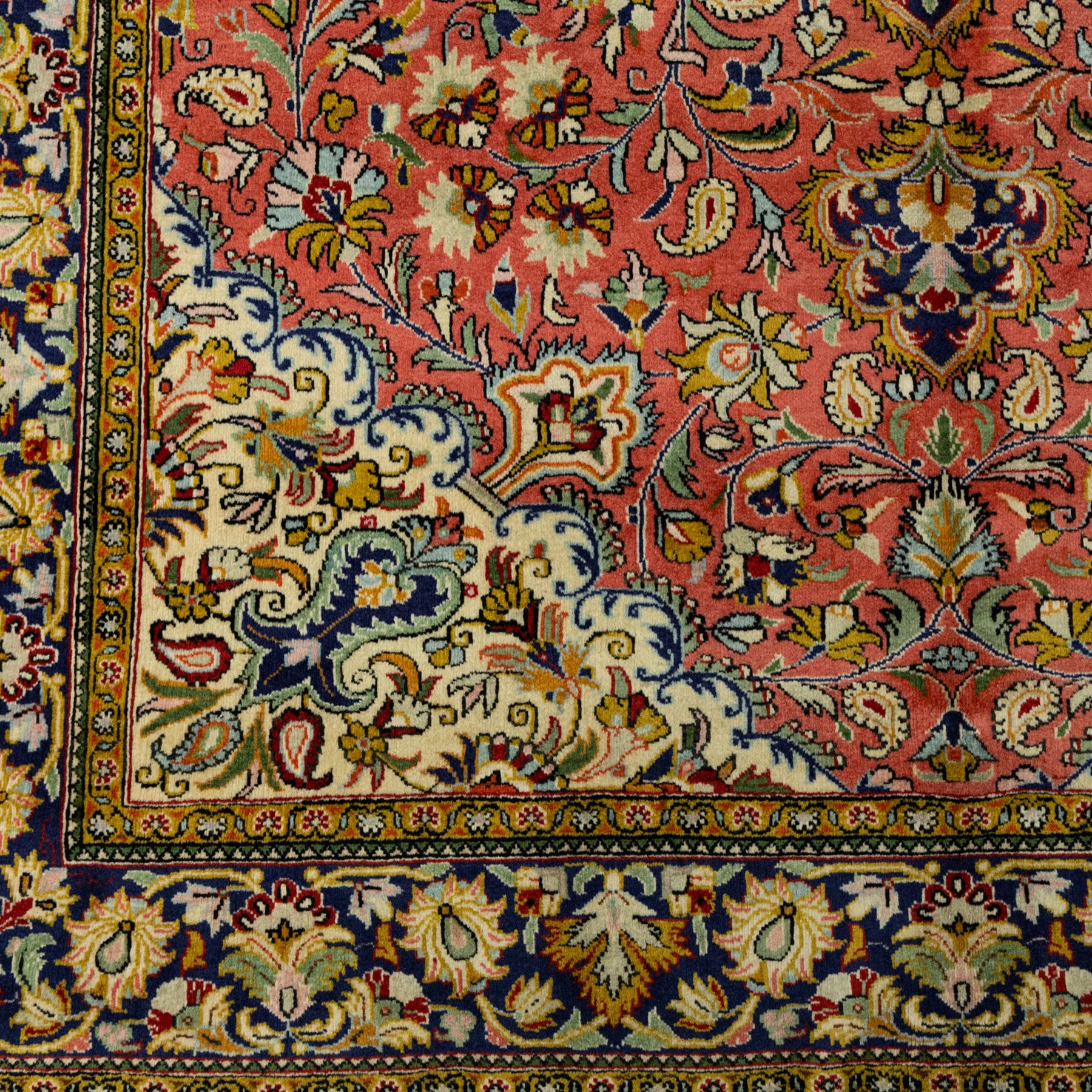 Central Persian Qom hand-knotted carpet, salmon pink ground, with a central dark navy shaped floral medallion with pendants, surrounded by dense scrolling foliate and floral motifs incorporating rosettes, palmettes and delicate vine work, enclosed by ivory spandrels and a dark navy border with repeating palmettes and meandering vines, flanked by narrow floral guard stripes, with cotton fringes