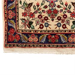 Two small rugs, an ivory ground example decorated with a central floral medallion and scattered rose sprays, enclosed by a navy foliate border (62cm x 101cm), and a crimson pictorial mat worked with seated figures, an animal and birds amongst flowering plants (45cm x 79cm) (2)