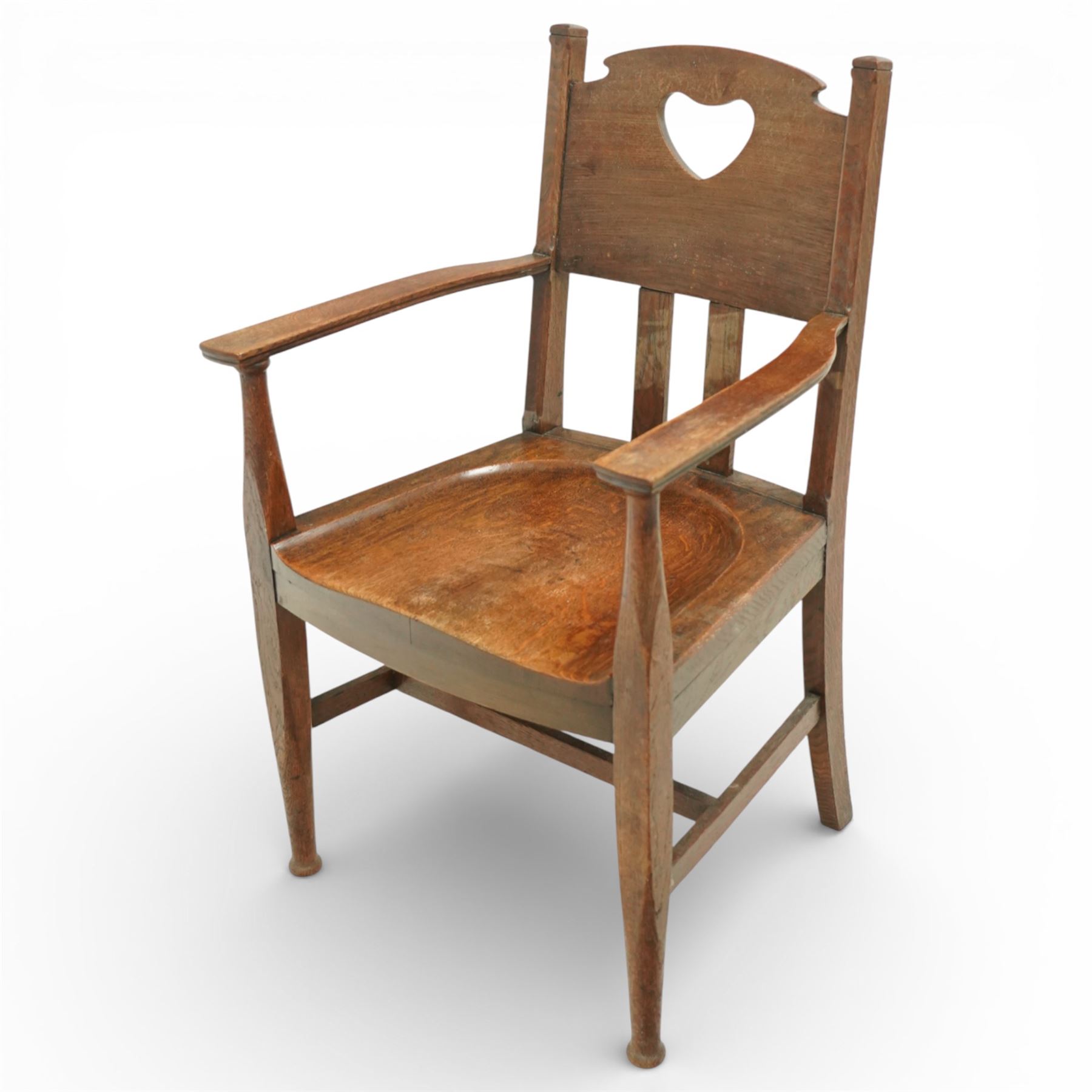 Arts and Crafts oak armchair, the shaped back with heart-shaped pierced splat above three vertical slats, solid dished seat with rounded front, open arms on turned front supports, square section legs united by plain stretchers
