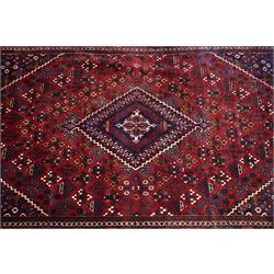 Central Persian Joshaghan hand-knotted carpet, deep red field decorated with a lattice design of stylized boteh and palmette motifs arranged around a stepped diamond medallion, navy corner spandrels similarly decorated enclosed by a dark indigo main border of floral and geometric motifs between multiple guard stripes, with cotton fringe ends 