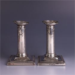 Pair of late Victorian silver mounted candlesticks, the stems embossed with classical ribbon and swag design, upon weighted stepped square bases, hallmarked London 1899, maker's mark worn and indistinct, H12cm