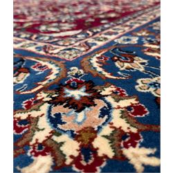 Central Persian Yazd hand-knotted rug, madder red field with scrolling vines, palmettes, and rosettes around a cusped lozenge medallion within a blue ground border of palmettes and flowerheads, 366cm x 250cm