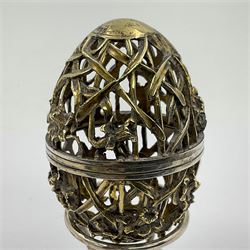 Modern silver limited edition Easter egg, no. 70/500, the gilt openwork body decorated with daffodils and detachable cover with pierced circular panel set with a single faceted blue stone, opening to reveal a gilt interior, upon silver stand with three scrolling pad feet, each hallmarked St James House Company, London 1980, height including stand 8cm