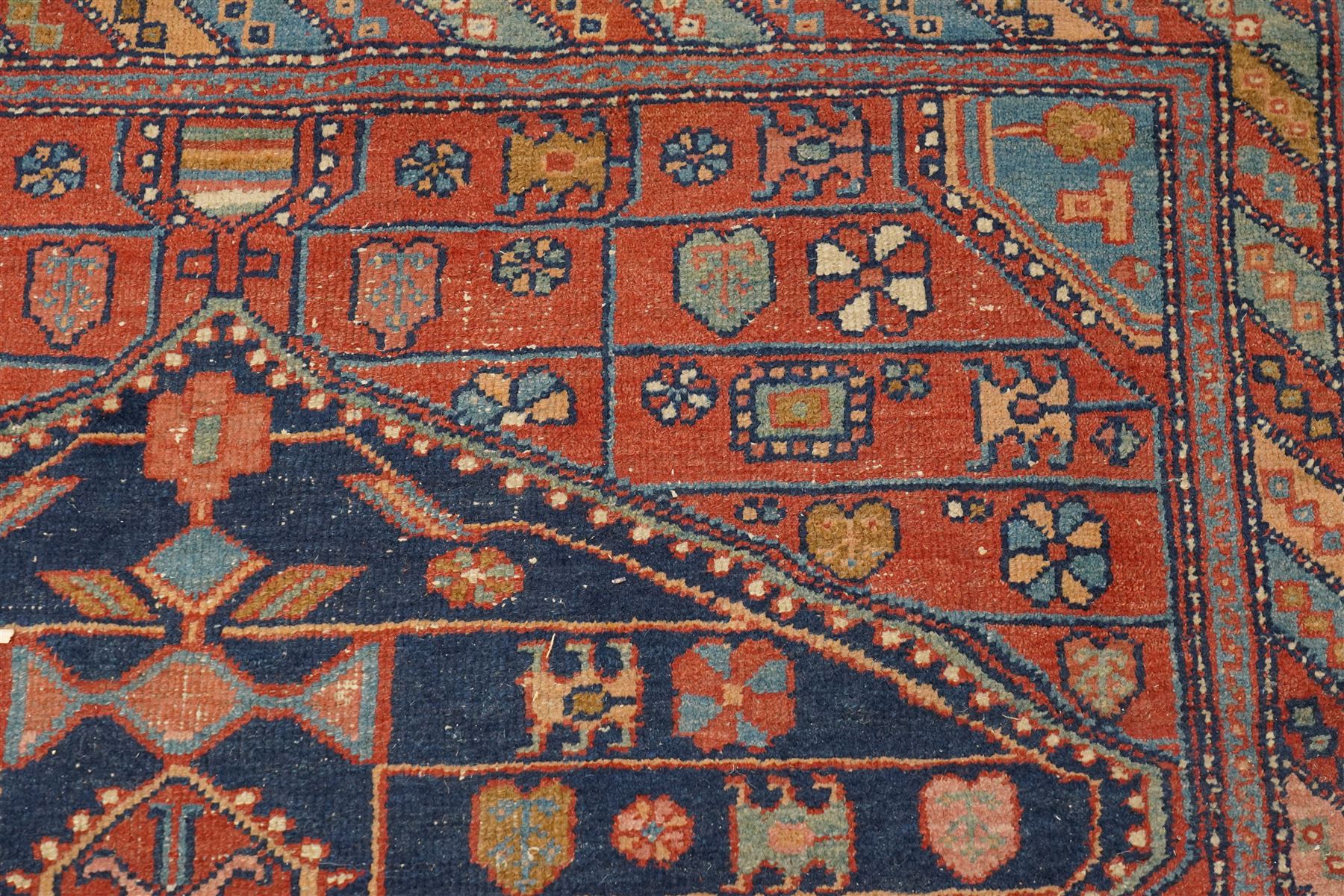 Persian Heriz hand-knotted carpet, terracotta ground centred by large dark navy geometric medallion with stepped outline, decorated throughout with stylised flowerheads, palmettes and geometric motifs in blue, green and ochre, enclosed by diagonal geometric border with narrow guard stripes