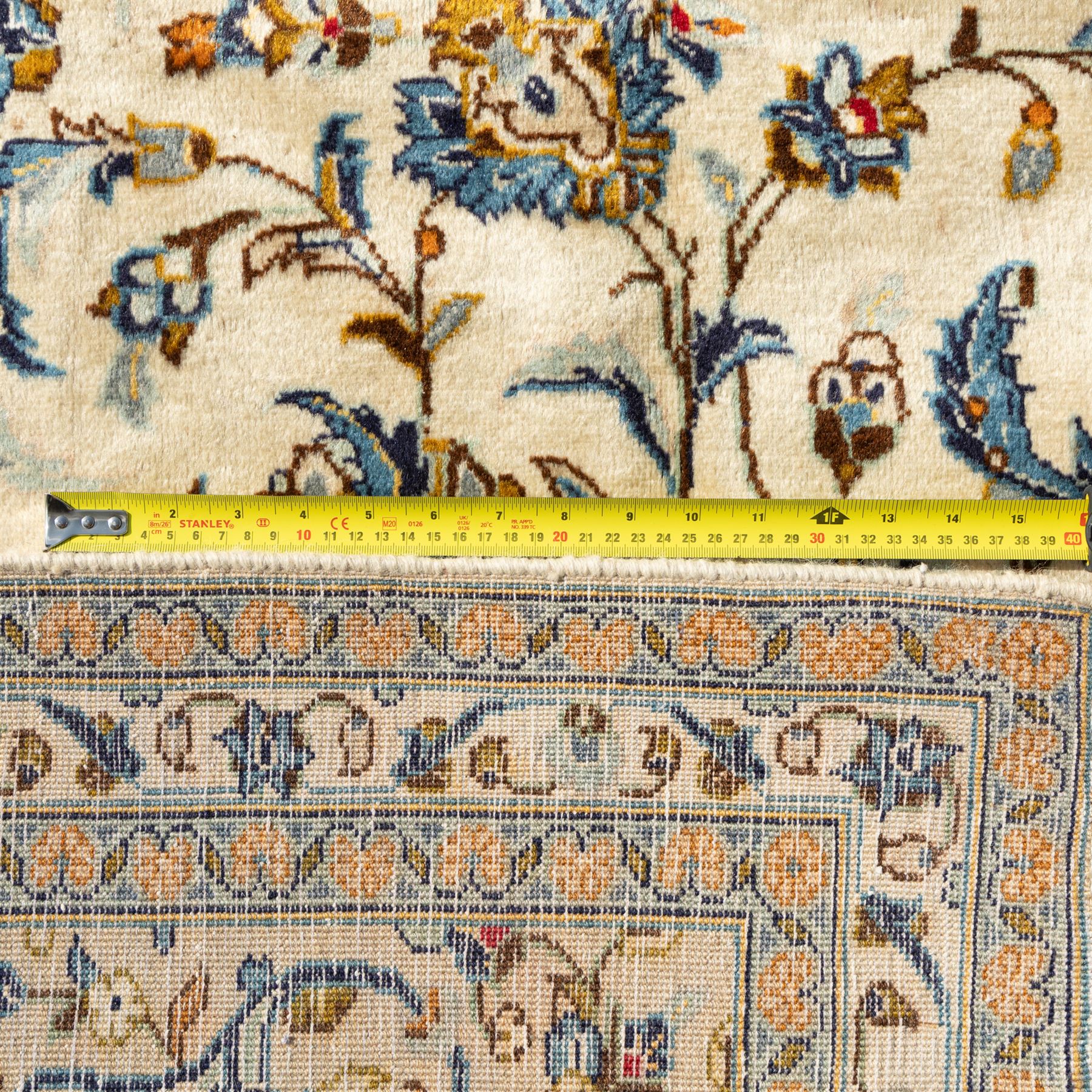 Central Persian Kashan rug, cream ground densely patterned with interlaced floral stems and rosettes in blue, gold and brown, framed by layered borders featuring stylised palmettes, woven in the Kashan weaving district of Iran