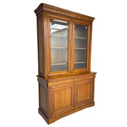 French cherry wood bookcase on cupboard, projecting cornice over two cupboard doors with bevelled glass panels enclosing three adjustable shelves, base fitted with two cushion drawers over double cupboard