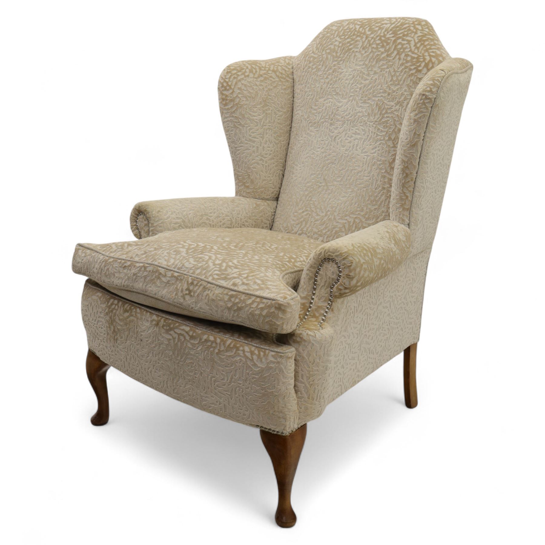Late 20th century wingback armchair, upholstered in beige embossed fabric with brass stud edging, on cabriole legs and splayed rear legs