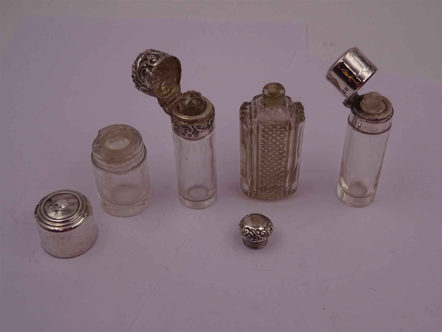 Four silver mounted glass scent bottles, including a Victorian cut glass example with embossed silver cover, and three cylindrical plain glass examples, on with engine turned decoration, three with glass stoppers, together with a pair of silver salts and spoons, all hallmarked, tallest H8cm