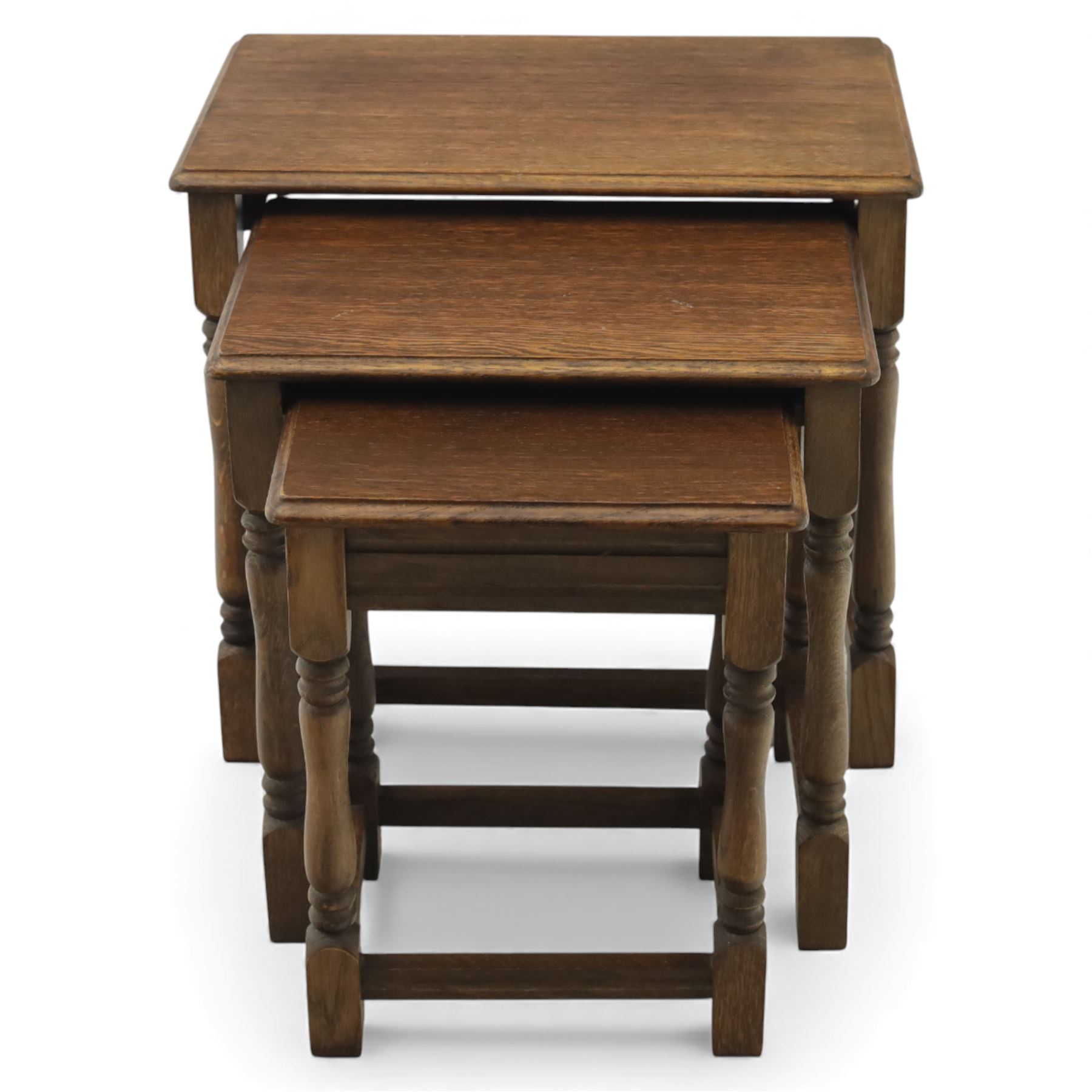 Nest of three dark oak tables, rectangular top with turned supports, tables suspended on rails