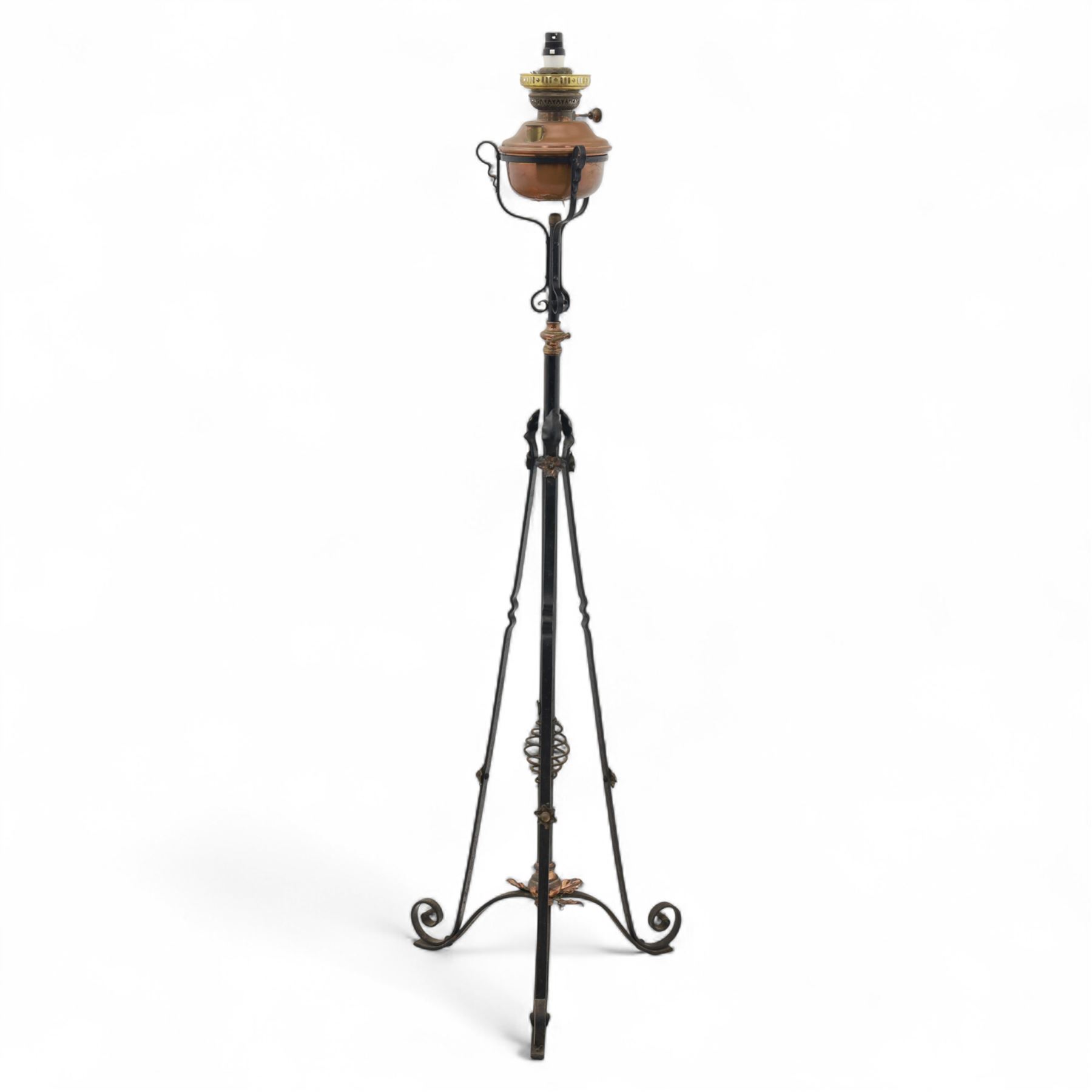 Early 20th century converted oil lamp standard, with copper reservoir and brass burner mount, later wired for electricity, on wrought iron tripod stand with scroll and twist ornamentation