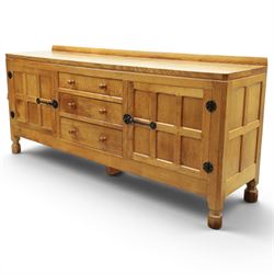 Mouseman - large adzed light oak sideboard, the rectangular top with raised galleried back, fitted with three central drawers flanked by panelled cupboards enclosing shelves, with wrought iron fittings, raised on octagonal feet, with signature carved mouse, by the workshop of Robert Thompson, Kilburn