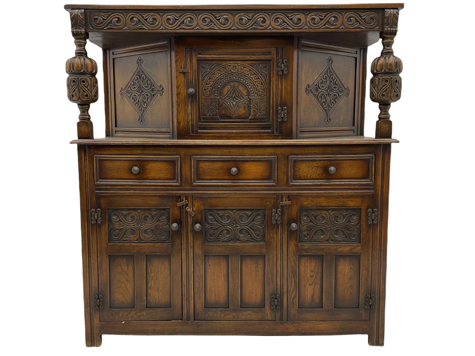 20th century carved oak court cupboard, s-scroll carved frieze over panelled cupboard door carved with arch, lobe and scroll carved cup and cover supports, fitted with three drawers and three cupboards below