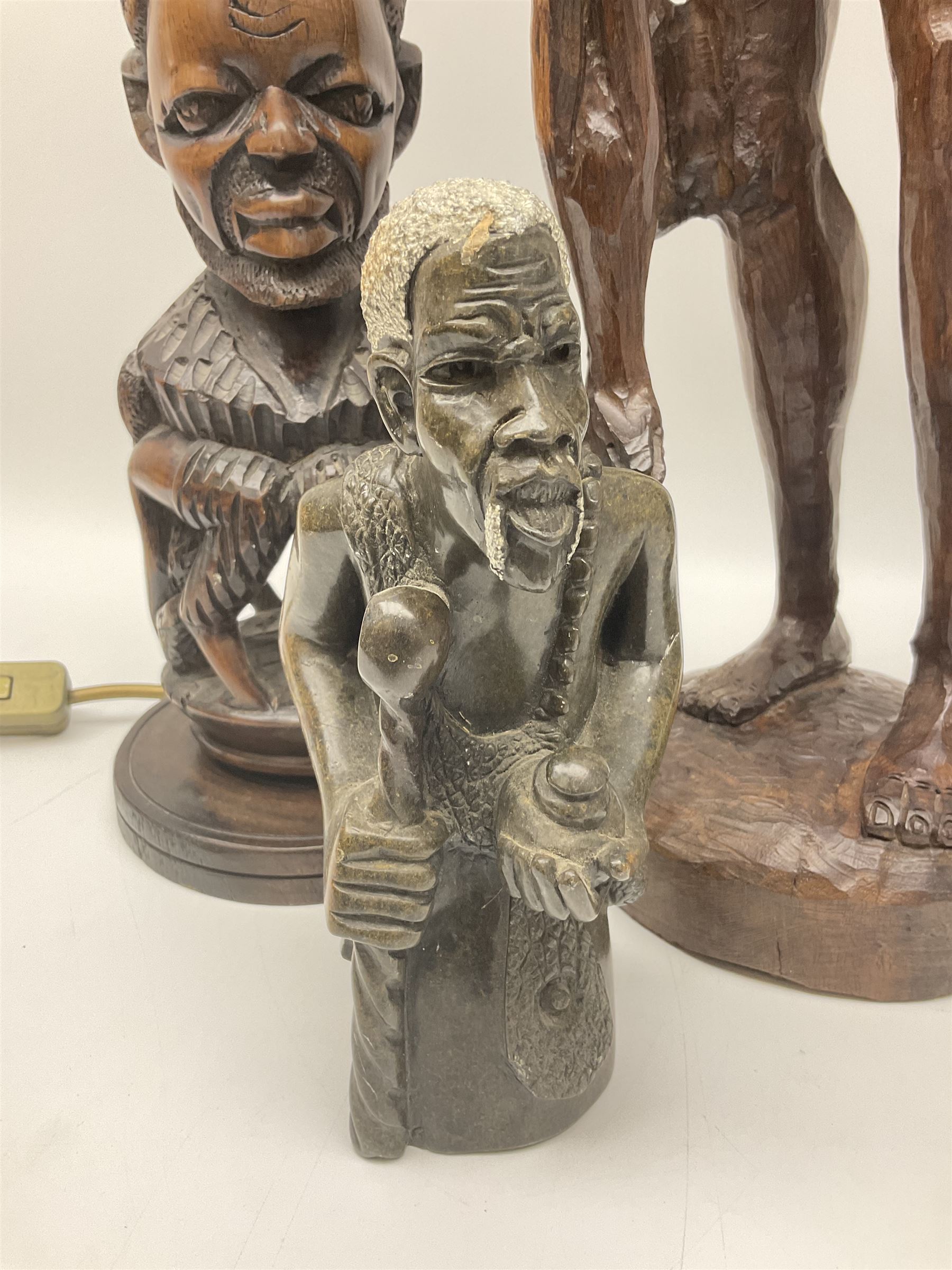 Pair of 20th century carved wood table lamp with African busts and figures, together with a carved wooden figure and soapstone figure, lamps H44cm