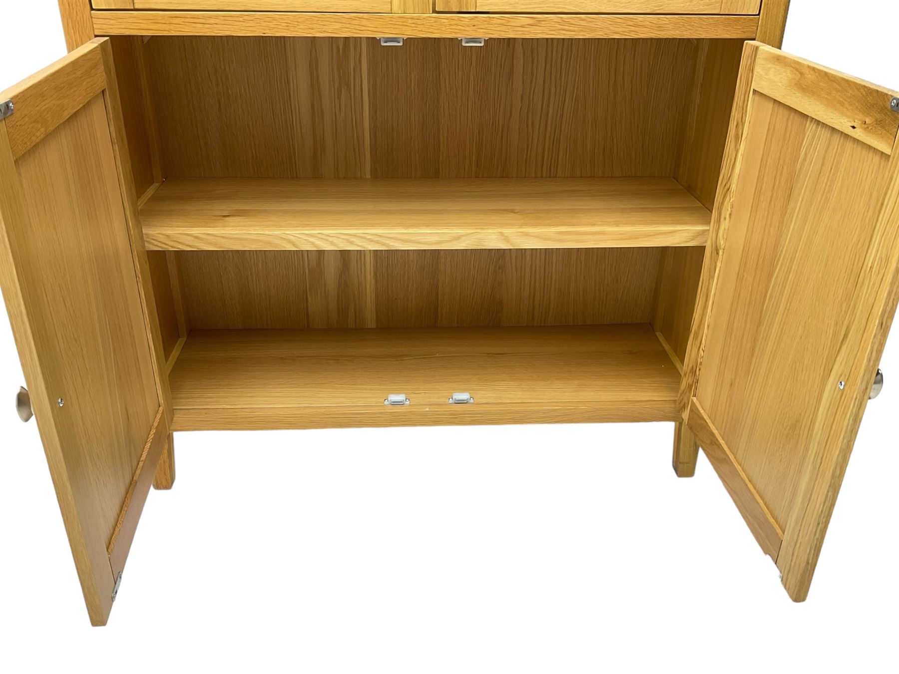 Contemporary light oak display cabinet on cupboard, fitted with two glazed doors enclosing two adjustable glass shelves with light fittings to the top, over panelled cupboard concealing single shelf, on square supports