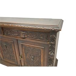 Victorian heavily carved oak sideboard, the moulded top carved with foliate decoration to the edge, fitted with two drawers and three cupboards, the drawer fronts carved with green man mask handles and scrolling foliage, the panelled doors carved with interlacing foliage, on turned compressed bun feet