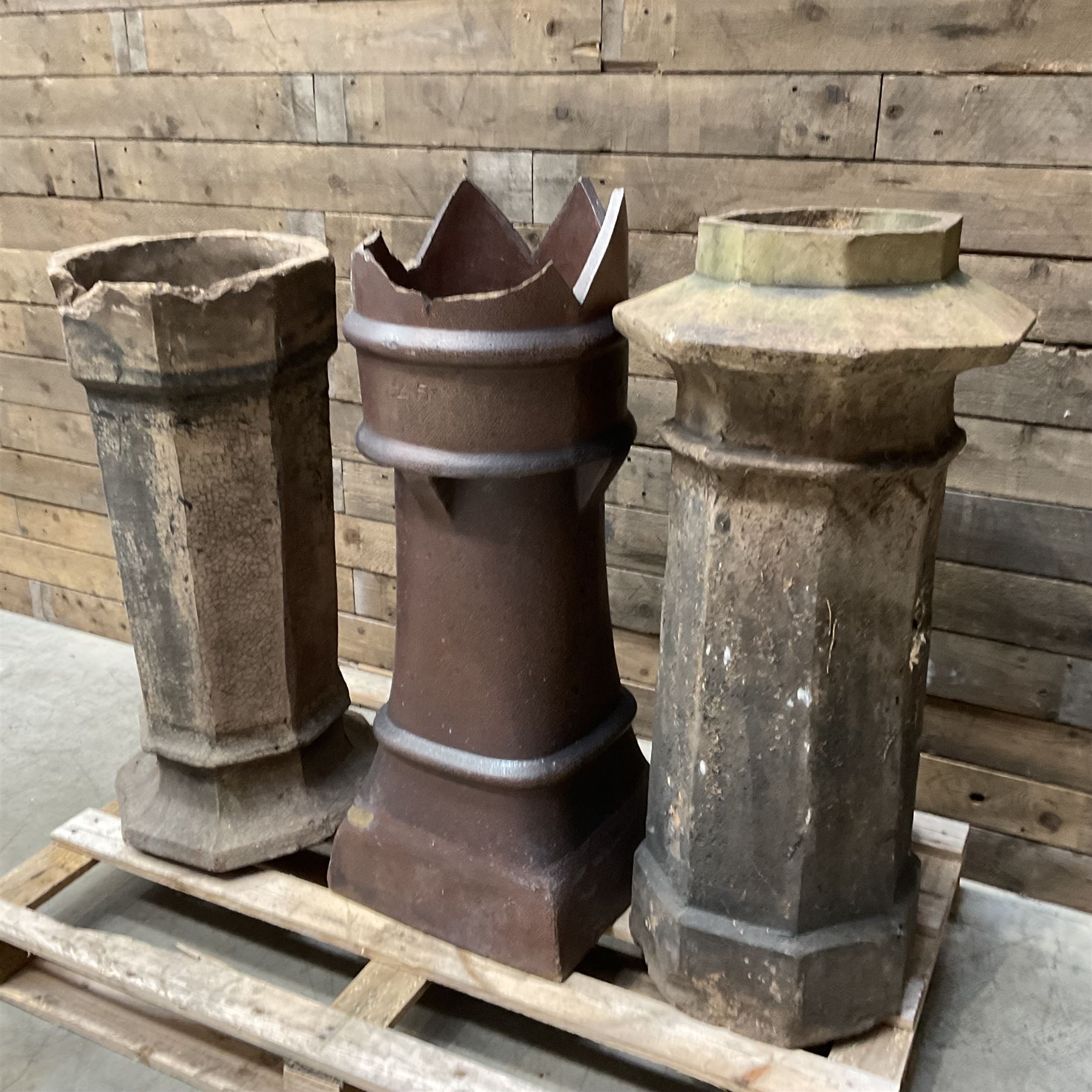 Collection of three Victorian and early 20th century reclaimed terracotta chimney pots, comprising: one cylindrical form with weathered, cracked glaze and flared octagonal base; one deep red cylindrical pot with fluted midsection and castellated rim, bearing moulded number ‘25’; and one tapering hexagonal example with wide flared rim and weathered patina. All with age-related wear and chips, consistent with use and outdoor exposure. Plus a selection of cast stone pieces including fountain 
