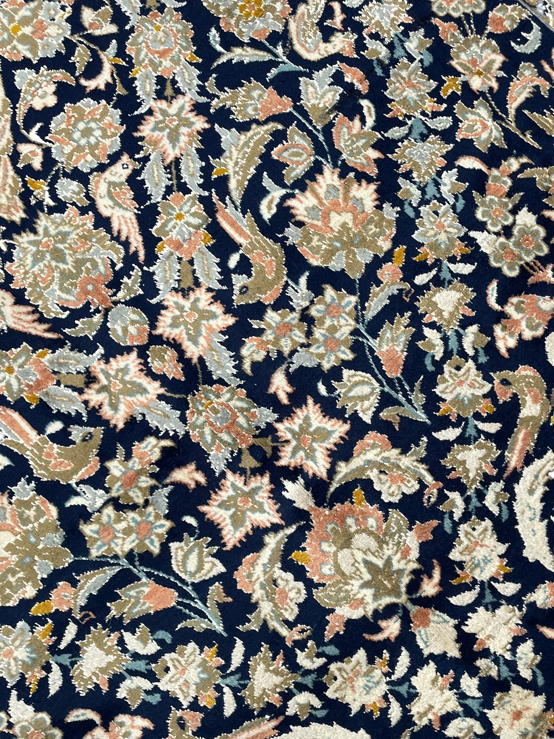 Persian Kashan indigo ground rug, the field consisting of trailing flower head bands and leafy branches, decorated with kuş or bird motifs, the border with repeating border containing curling leaves and flower heads, within guard bands 