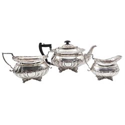 Edwardian three piece silver tea service, comprising teapot with ebonised handle and finial, twin handled open sucrier, and milk jug, each of oval part fluted form with cast foliate rims, upon four scroll mounted paw feet, the teapot with engraved dedication, hallmarked Thomas Bradbury & Sons, London 1905, approximate total weight 46.88 ozt (1458 grams)