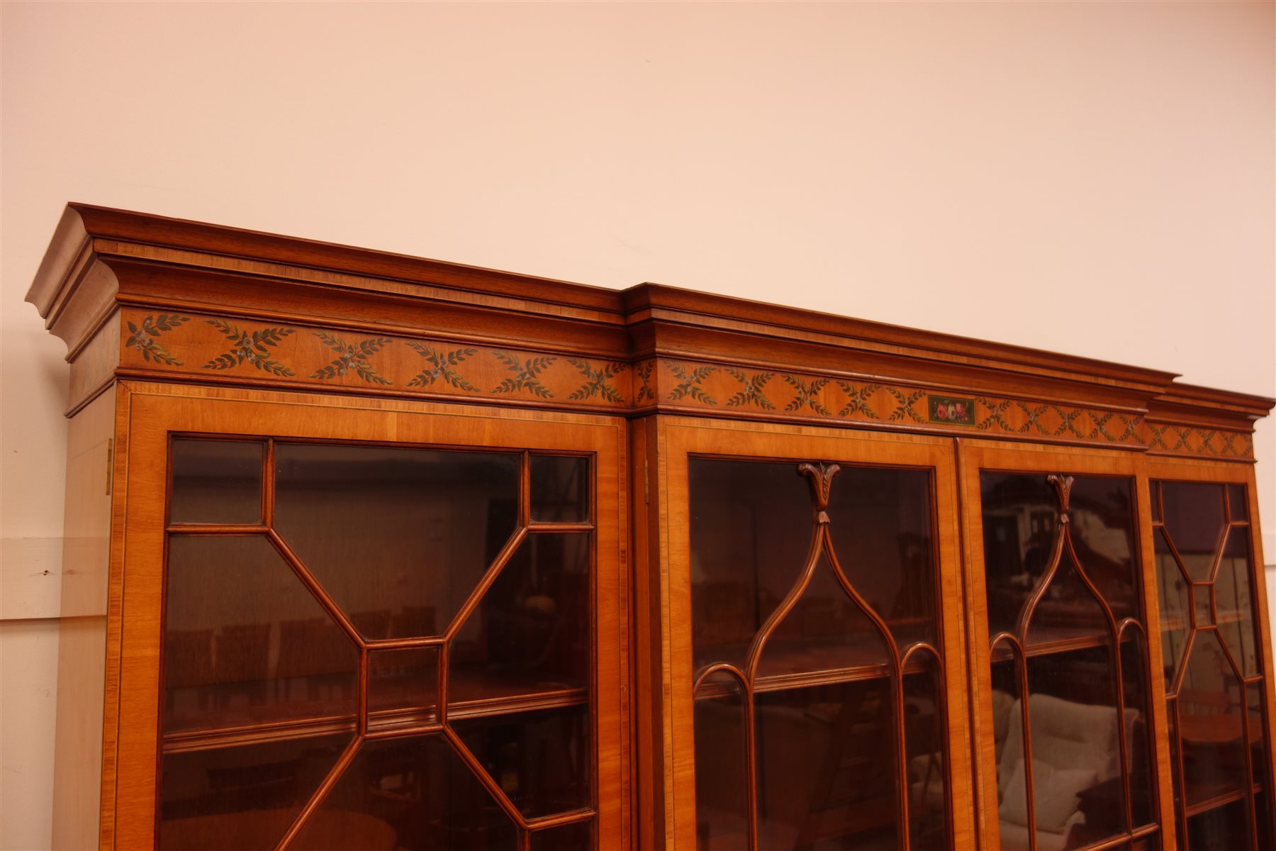 Sheraton Revival satinwood breakfront bookcase, frieze painted with scrolling leafage above four astragal doors with adjustable shelves, the base with four doors painted with floral sprays in oval panels, on a plinth base, W234cm, H235cm, D52cm