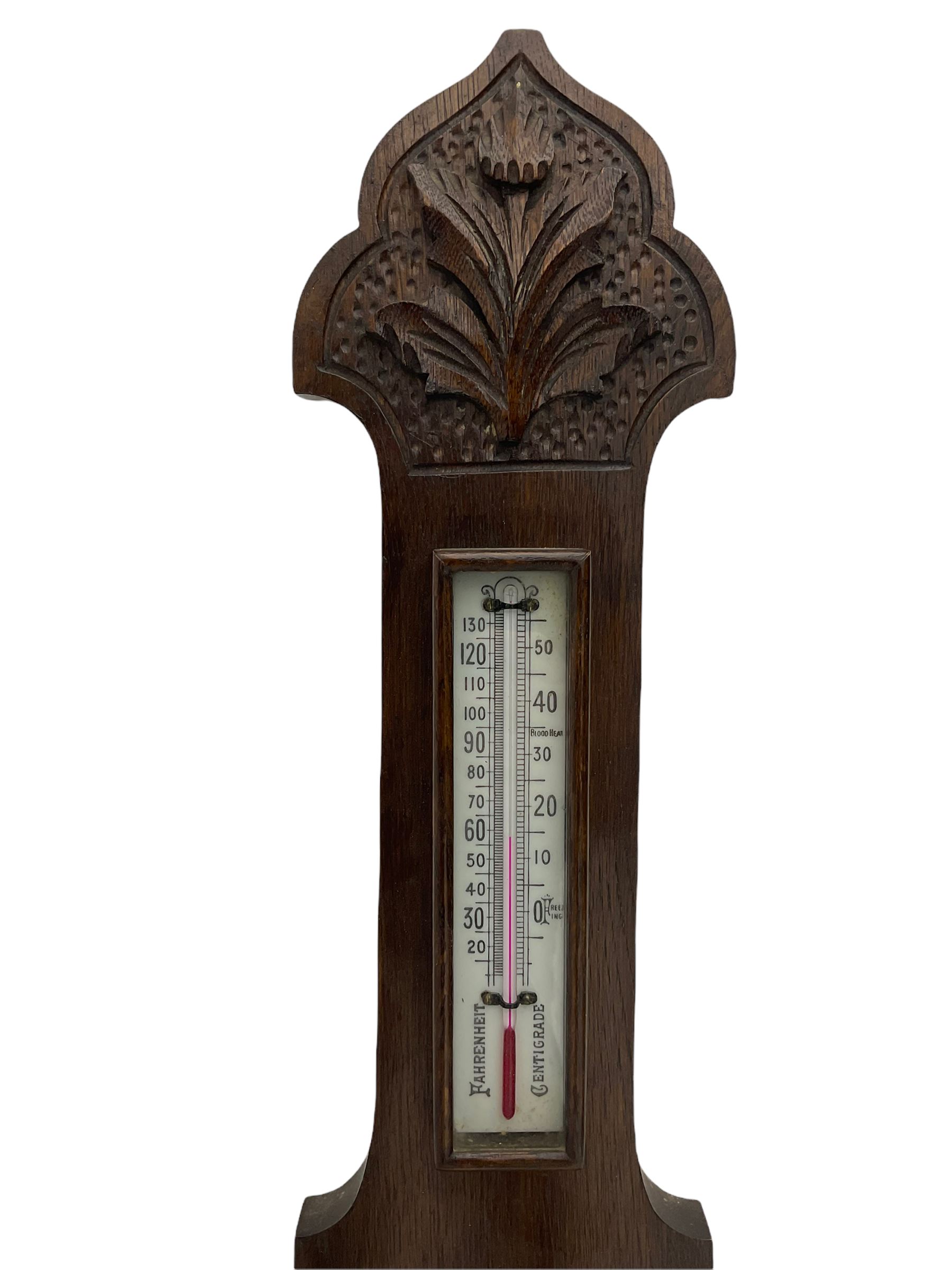 An English carved oak cased aneroid barometer with an 8'' porcelain dial, measuring barometric pressure from 26 to 31.9 inches, weather predictions written in gothic capitals and lower-case script, with a steel indicating hand and brass recording hand within a chrome bezel with a flat bevelled glass, with a spirit thermometer recording the temperature in degrees Fahrenheit and Celsius.



