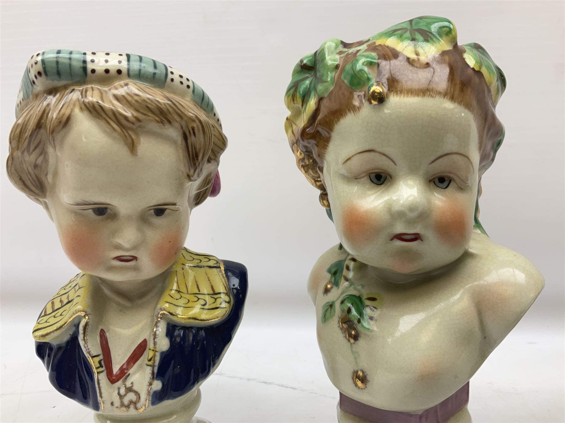 19th century pair of hand painted ceramic busts of children, together with a third similar example of a putti with a crown of ivy, tallest H23cm 