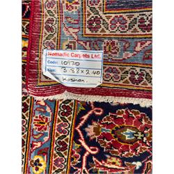 Central Persian Kashan hand-knotted carpet, the madder red field with central lobed medallion in indigo and ivory, enclosing scrolling arabesques and flowerheads, framed by palmette spandrels and an indigo border of rosettes and lotus forms between multiple floral guard stripes, from the region of Kashan