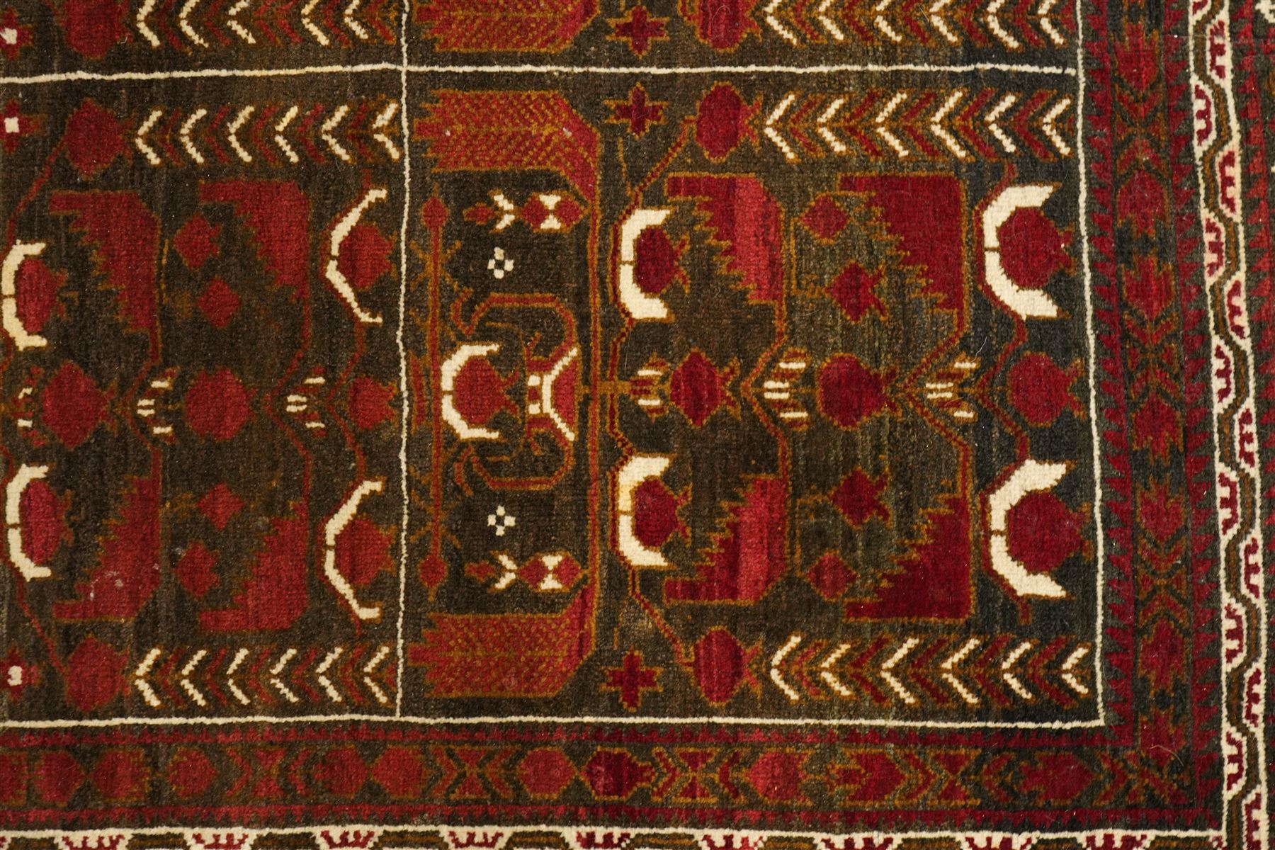 Baluchi hand-knotted prayer rug, dark brown ground divided into six panels decorated with stylised tree-of-life and flowering motifs in madder red and ivory, enclosed by multiple narrow geometric borders, with fringed ends