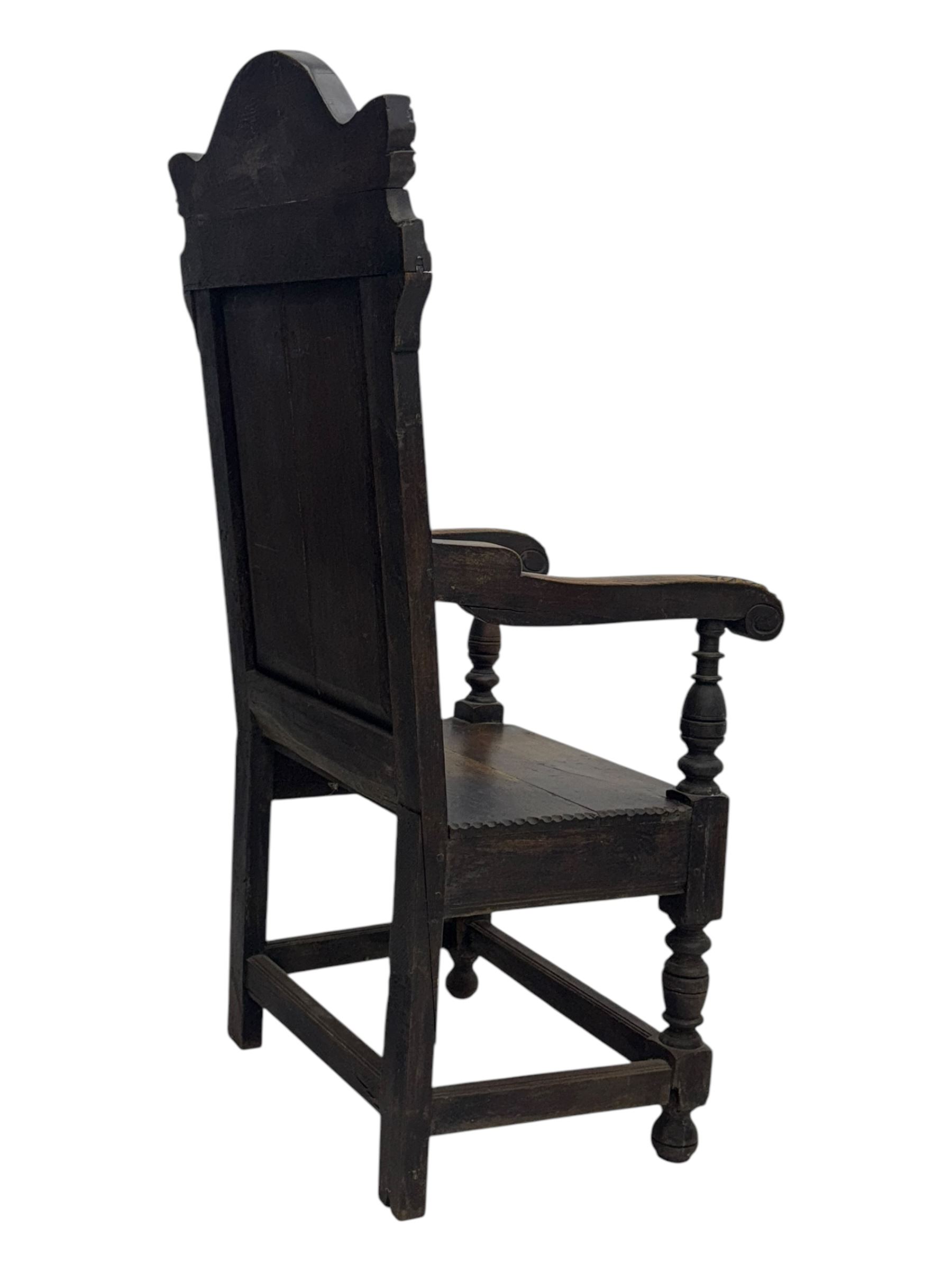 Late 19th century Jacobean revival carved oak armchair, the tall back with arched cresting featuring a stylised foliate mask, flanked by carved scrolls, relief carved panel depicting symmetrical foliage, downscrolled arms, on turned front supports united by stretchers