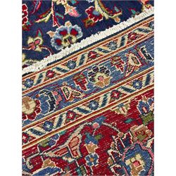Large Persian Kashan carpet, red and blue ground, the field with central medallion surrounded by interlacing foliate and plant motifs, the border with scrolling design and decorated with flower heads