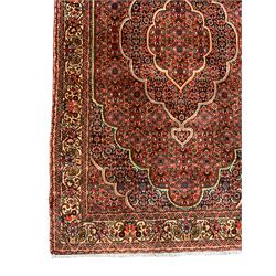 Persian Bidjar crimson ground rug, thick woollen pile, the field decorated with repeating Herati motifs within cusped outlines, the guarded border decorated with repeating flower head motifs