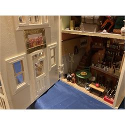 Seagull Pub - scratch-built wooden doll's house as a two-storey gable fronted public house painted in white green and maroon; the hinged front with ground floor veranda and window over opening to reveal two fully furnished rooms with dog-leg staircase and well stocked bar with bar-tender L31cm H62cm D37cm; together with Corner Shop and Dollies Pantry; a similarly painted scratch-built wooden two-storey flat-roofed doll's house as a well stocked ground floor grocery shop with stairs up to two further fully furnished rooms and more stairs giving access to a roof terrace L46cm H57cm D33cm (2)