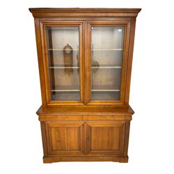 French cherry wood bookcase on cupboard, projecting cornice over two cupboard doors with bevelled glass panels enclosing three adjustable shelves, base fitted with two cushion drawers over double cupboard