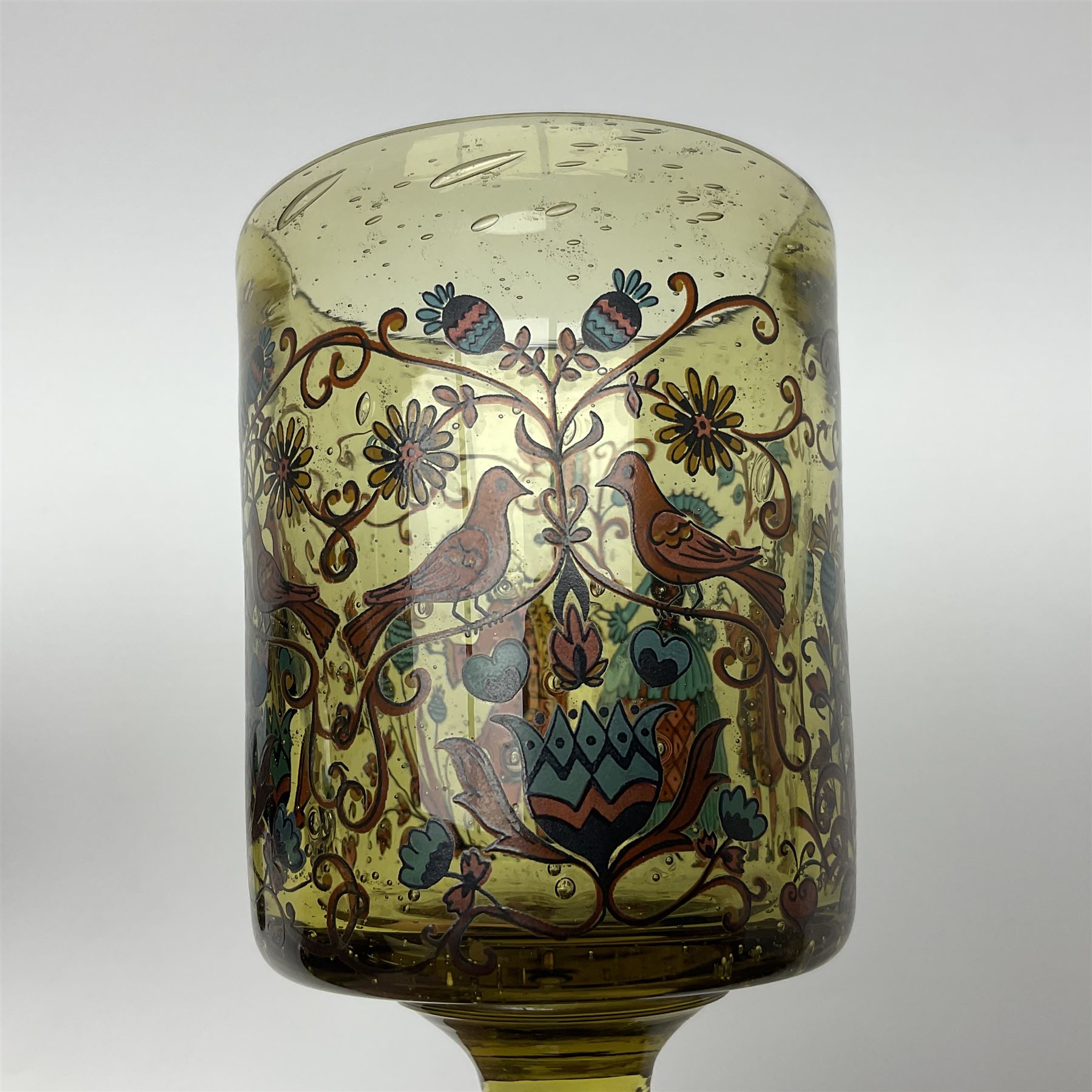 19th Century Bohemian amethyst glass lidded goblet, the bowl of faceted form, gilded with three children in period dress playing games, upon a knopped stem and conforming faceted foot, together with an art nouveau green glass goblet, with gilded rim, upon clear trumpet stem, and a hand blown wine glass, transfer printed with birds and three figures in period dress, tallest H29cm